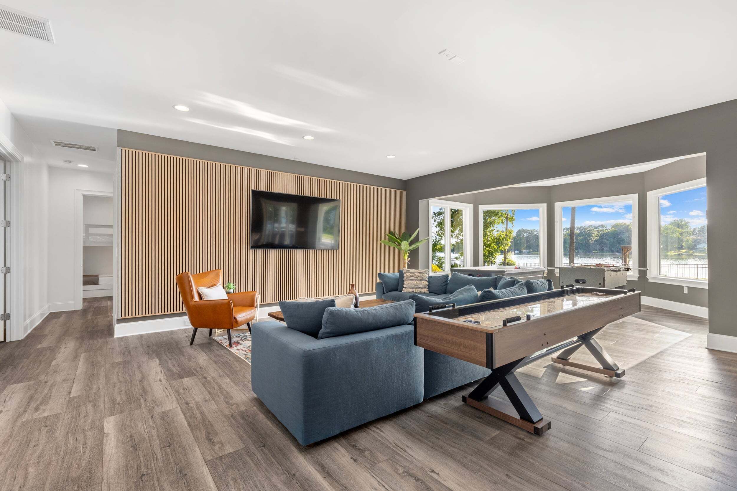 A modern living room with a pool table, a sofa, and a TV mounted on a wooden wall.