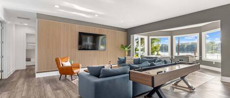 A modern living room with a pool table, a sofa, and a TV mounted on a wooden wall.