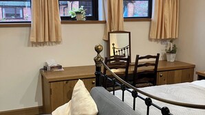 A bedroom with a bed, a grey sofa, a wooden desk, two windows with curtains, a mirror, and a potted plant. - Cottage in Nuneaton - Sleeps 2 - Parking - Garden (Nuneaton)