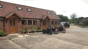 A brick building with a pitched roof, two motorcycles parked in front, and a car in the background. - Cottage in Nuneaton - Sleeps 2 - Parking - Garden (Nuneaton)