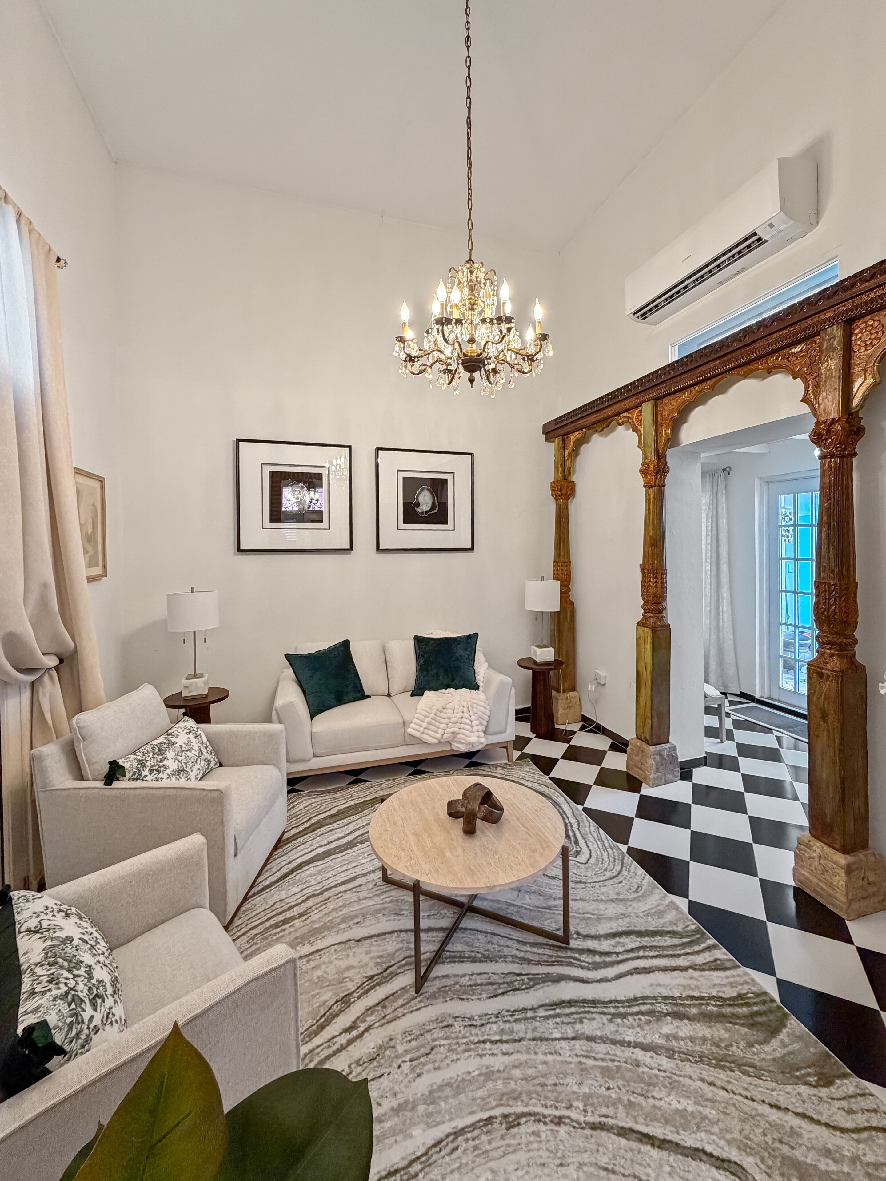 Uma sala de estar espaçosa com um lustre, um conjunto de sofá, uma mesa de centro e um chão quadriculado.