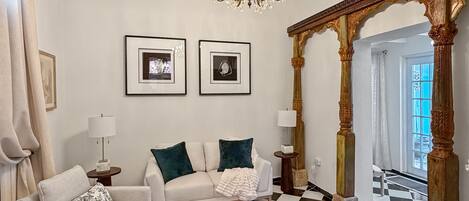 Uma sala de estar espaçosa com um lustre, um conjunto de sofá, uma mesa de centro e um chão quadriculado.