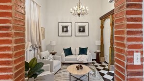 A living room with a chandelier, two framed pictures, a sofa, a coffee table, and a checkered floor. - Elegant Colonial Retreat in Mayagüez - 2BR/2BA (Mayagüez)