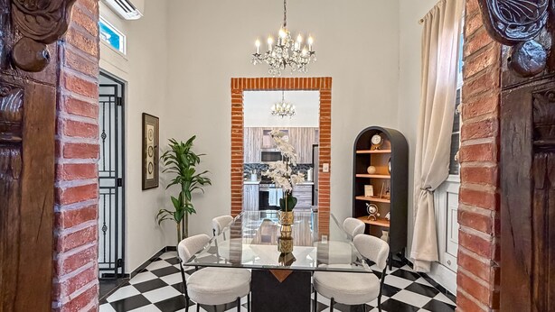 A dining area with a glass table, six chairs, a chandelier, and a checkered floor. - Elegant Colonial Retreat in Mayagüez - 2BR/2BA (Mayagüez)