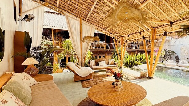 A spacious outdoor lounge area with a thatched roof, comfortable seating, and a pool. - Casa Alonia (Uluwatu)