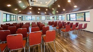 Ein Konferenzraum mit roten Stuhlreihen, Holzböden und großen Fenstern.