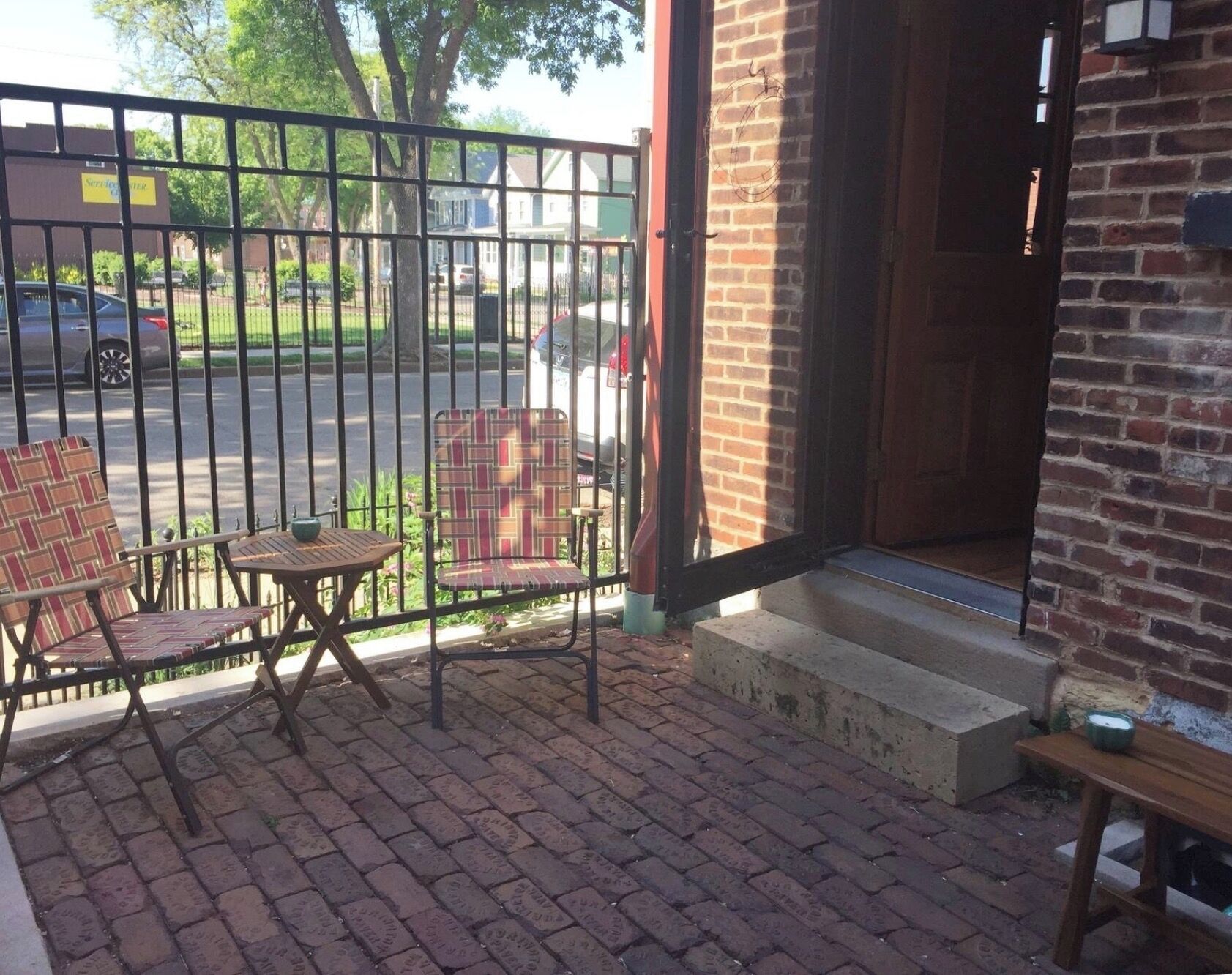 A patio with two chairs and a small table, a brick wall, and a metal gate.
