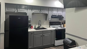 Una cocina compacta con armarios blancos, un refrigerador negro, una estufa y un lavabo.