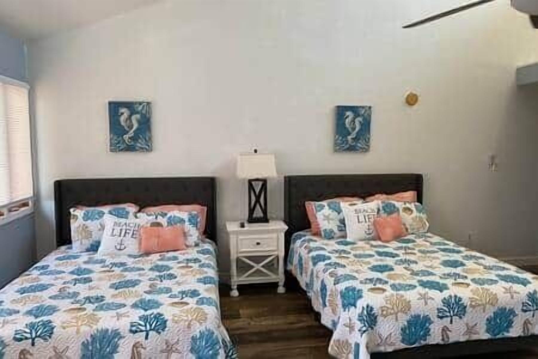 A bedroom with two beds, each with a floral bedspread and matching pillows. There are two nightstands with lamps between the beds.