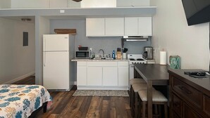 Cocina compacta con refrigerador, microondas, estufa y pileta. Cuenta con un ventilador de techo y un televisor montado en la pared.