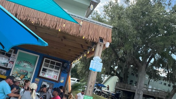 Restaurante com mesas ao ar livre, toldo azul e aviso sobre a obrigatoriedade de coleiras para animais de estimação.