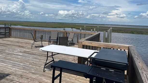 A wooden deck with a table and chairs, overlooking a marshy landscape.