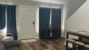 A living room with a ceiling fan, a brown couch, a wooden table with bar stools, and a door with curtains.