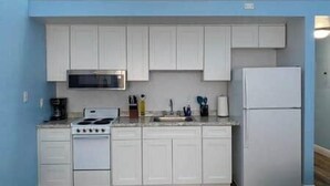 A compact kitchen with white cabinets, a stove, a microwave, and a refrigerator. - Legend Oaks room 4 over the water (Gautier)