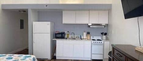 A compact kitchen with white cabinets, a refrigerator, a stove, and a microwave.