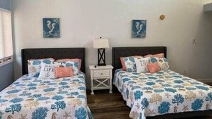 A bedroom with two beds, each with a floral bedspread and matching pillows. There are two nightstands with lamps between the beds. - Legend Oaks room 4 over the water (Gautier)