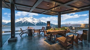 Un espace extérieur aménagé, abrité et doté de sièges, offrant une vue sur des montagnes enneigées et un lac.