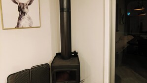 A room with a black wood-burning stove, a framed picture on the wall, and a sliding glass door leading to an outdoor area. - Caravan and house set up for mountain biking (Warburton)