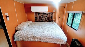 A compact bedroom with a bed, an air conditioner, a window with a view, and a suitcase. - Caravan and house set up for mountain biking (Warburton)