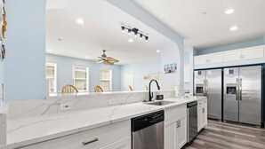 A modern kitchen with white cabinetry, a built-in dishwasher, stainless steel appliances, and a ceiling fan. - Tropical Castle | 12BR Retreat w/ Pool | Sleeps 50 (North Myrtle Beach)