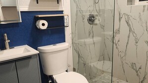 Een badkamer met een toilet, een douche met glazen deur, een wastafel en een spiegel.