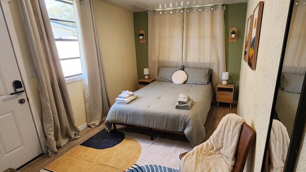 Een netjes ingerichte slaapkamer met een bed, nachtkastjes, een spiegel en een raam met gordijnen.