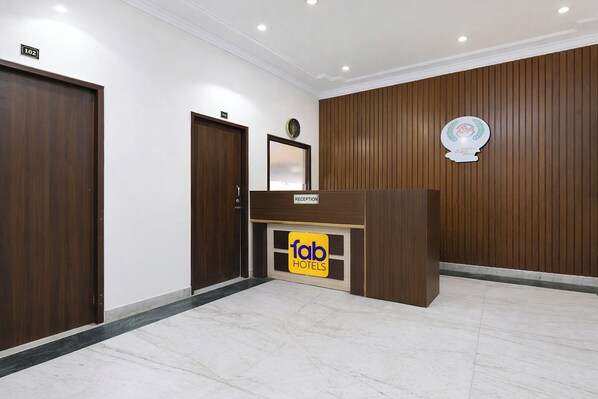 A hotel reception area with a wooden reception desk, a reception sign, and a wall-mounted emblem. - Fabhotel Royal Palace I (Jaipur)