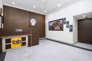 Zona de recepción de un hotel con un mostrador de madera, un cartel de 'fab hotels' y una pared decorada con cuadros.