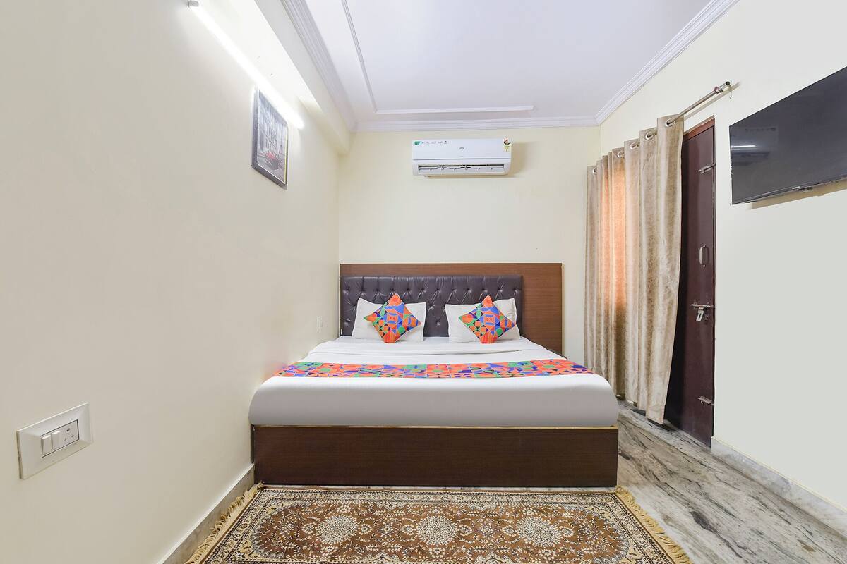 Habitación de hotel ordenada con cama, un tapete estampado, equipo de aire acondicionado y una puerta con cortinas.