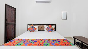 A bedroom with a bed, two pillows, a colorful bedspread, a wardrobe, an air conditioning unit, and a small table. - Via Kanha Shiva (Ayodhya)