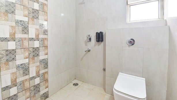 Et badeværelse med bruser, toilet og en flisevæg med et geometrisk mønster.
