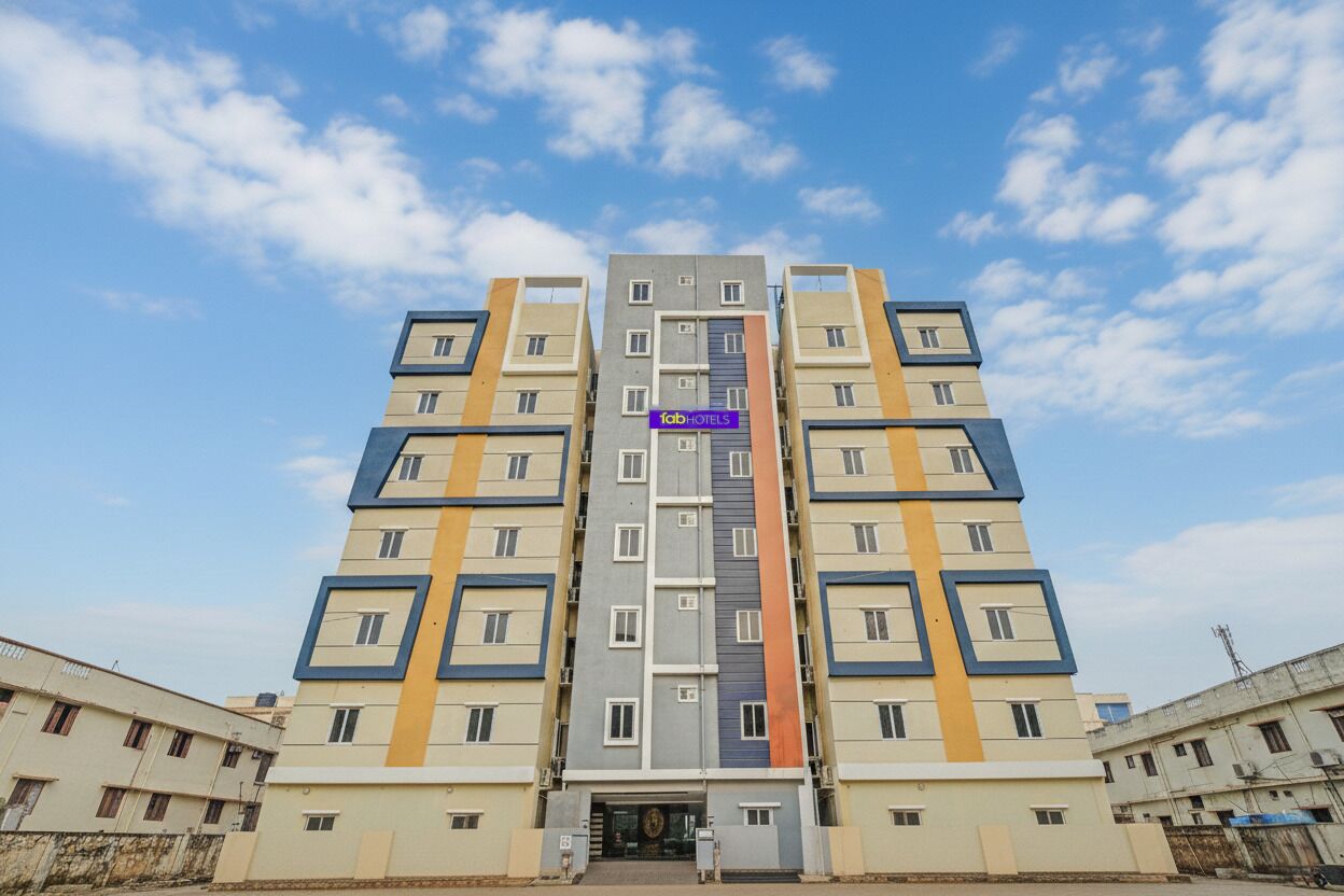 A multi-story hotel with a central entrance, balconies on each floor, and a clear sky.