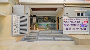 The entrance to Karthik's Elite PG, a co-living PG for men and women, with a signboard displaying amenities and location details.