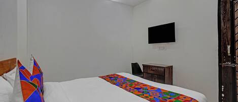 Un dormitorio con una cama, un televisor montado en la pared, una mesita de noche de madera y una puerta.