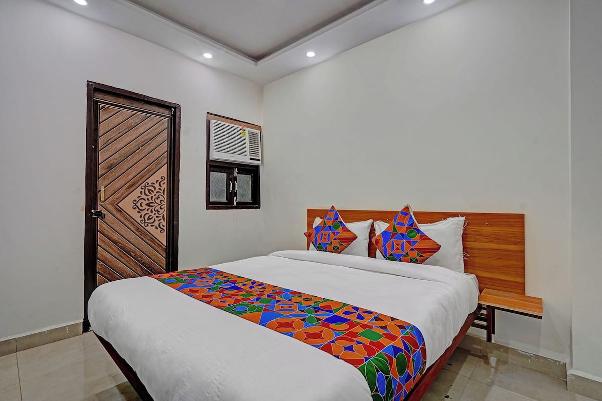 Un dormitorio con cama, una puerta de madera, un equipo de aire acondicionado y una ventana.