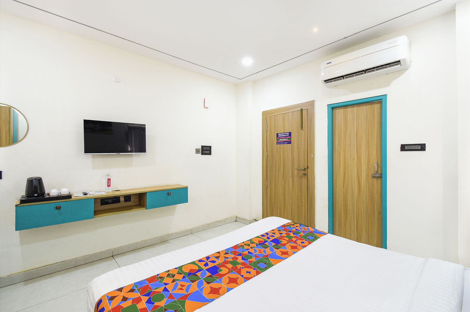 A hotel room with a bed, a TV, a minibar, a reception sign, and an air conditioner.