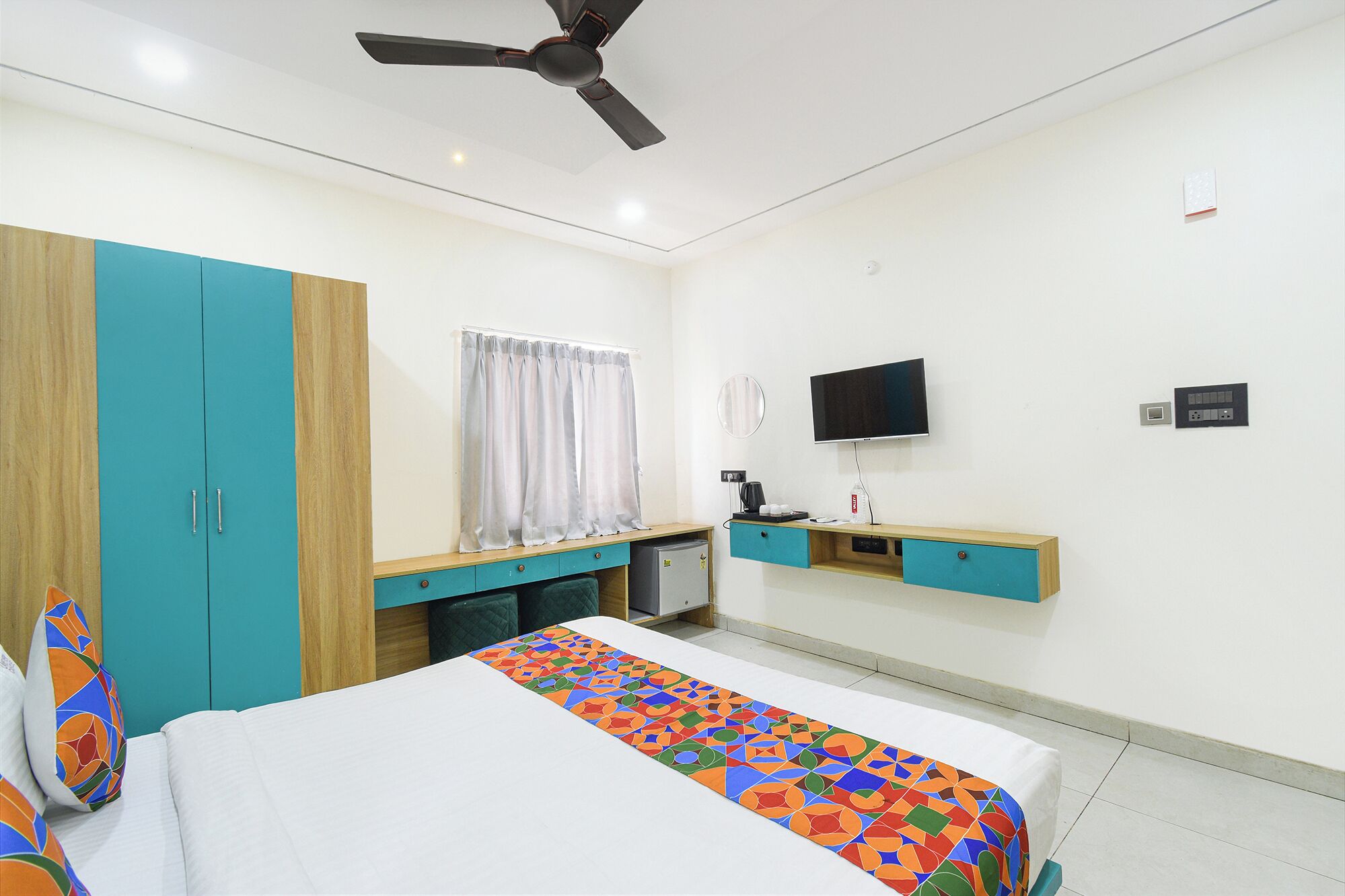 A hotel room with a bed, a desk, a TV, and a ceiling fan.