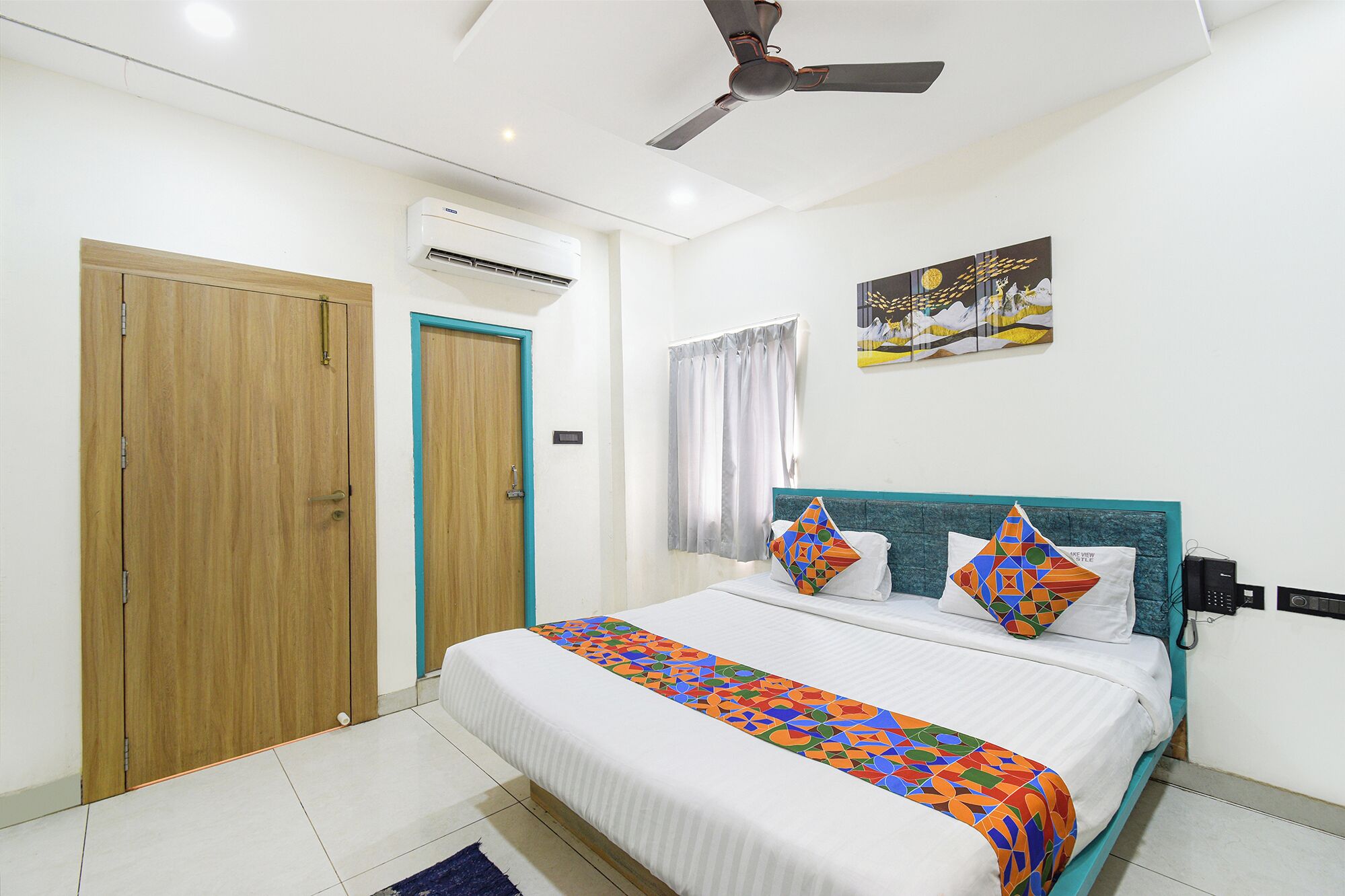 A bedroom with a bed, a ceiling fan, an air conditioning unit, a window with curtains, and a wall-mounted artwork.