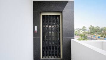 Entrada de um edifício moderno com uma parede texturizada escura, um portão de metal e uma pequena placa.