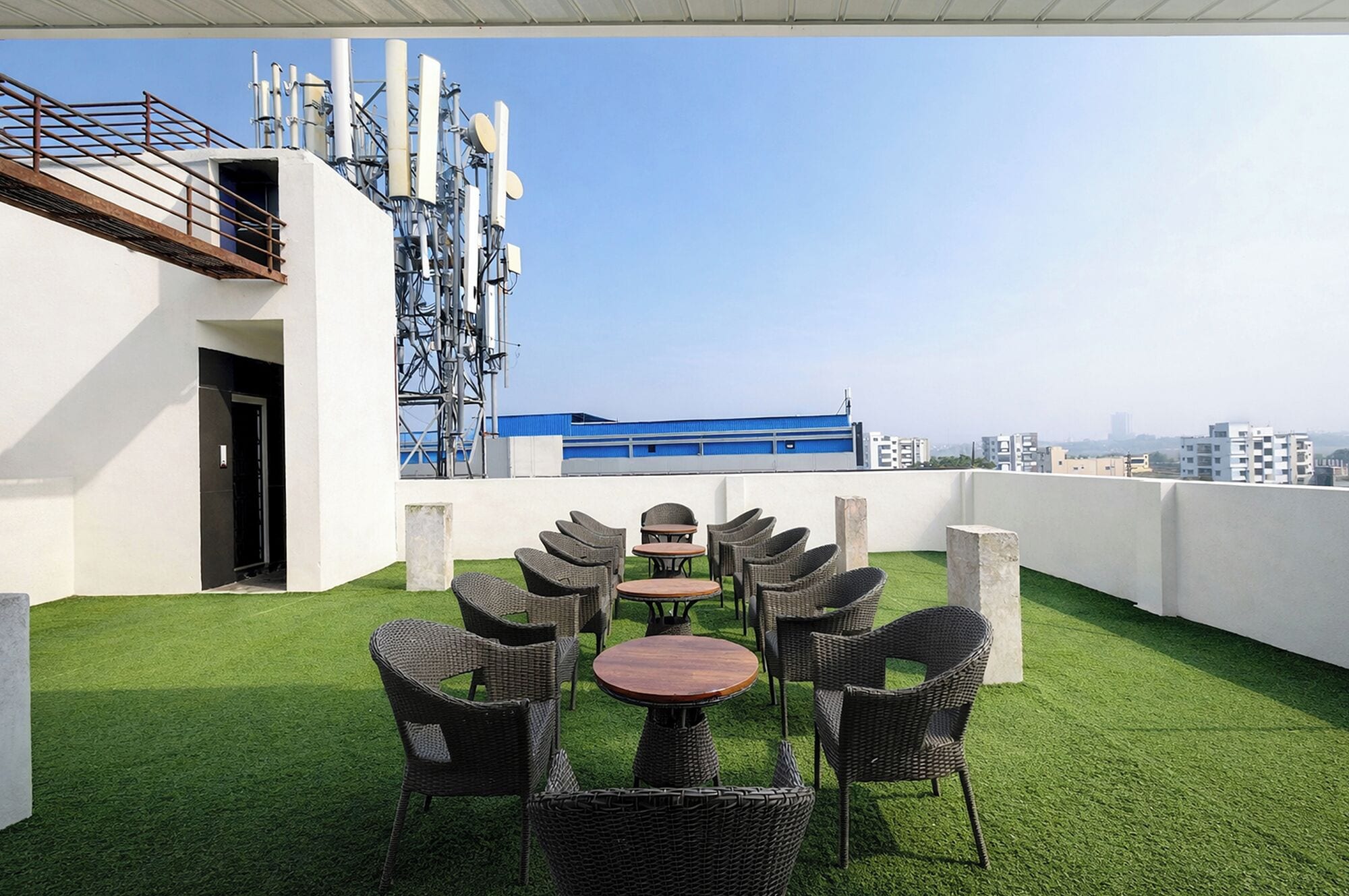 Een terras met rieten meubels en kunstgras, met uitzicht op een stadsbeeld.