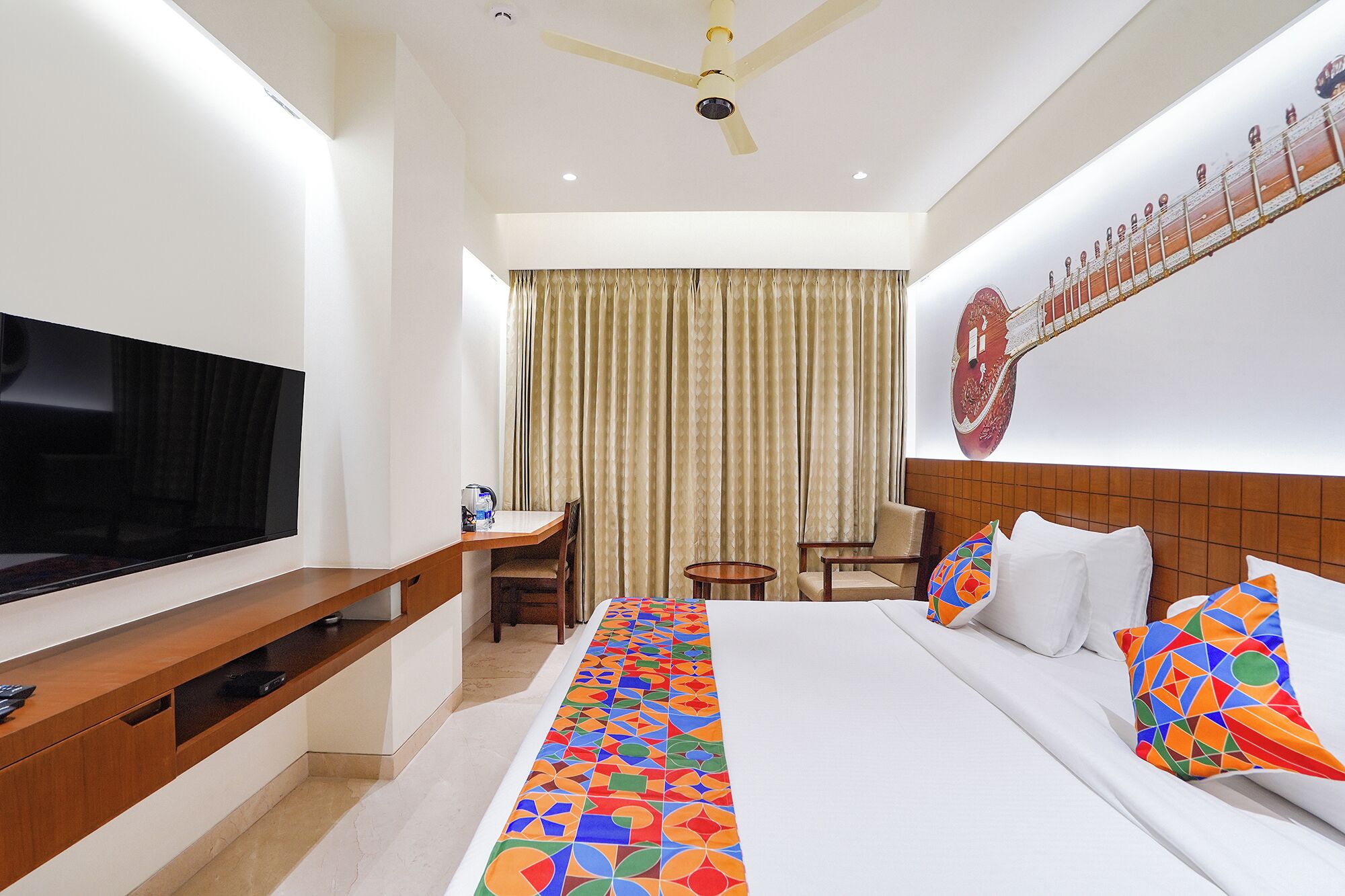 A hotel room with a bed, TV, desk, chair, and curtains.