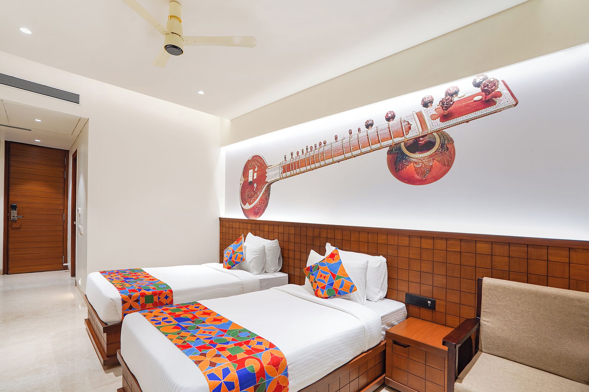 A hotel room with two beds, a wooden headboard, a ceiling fan, and a wall-mounted artwork of a stringed instrument.