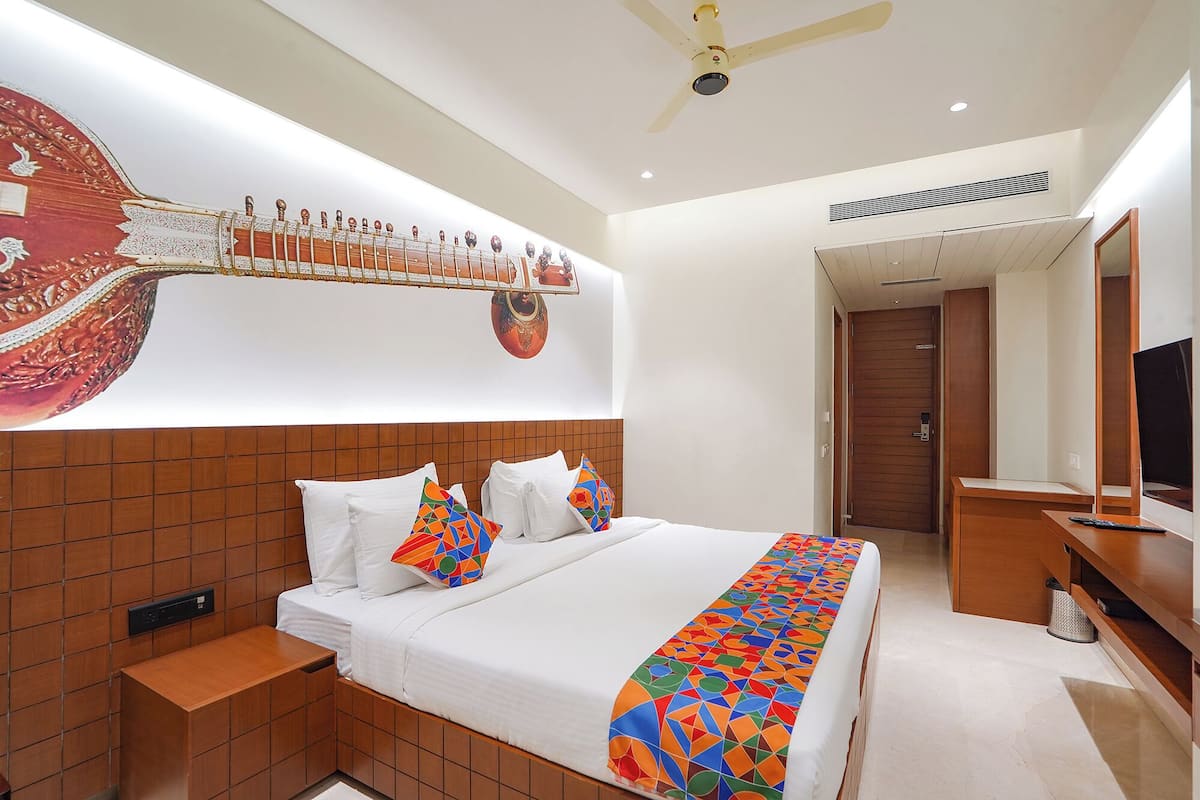 A hotel room with a large bed, a ceiling fan, a wall-mounted TV, and a wooden headboard.