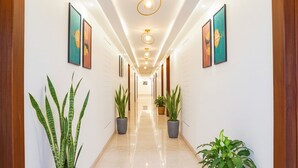 A hallway with a marble floor, potted plants, framed artwork, and recessed lighting. - Oriva Tulips Inn and Suites - Nr. Majestic (Bengaluru)