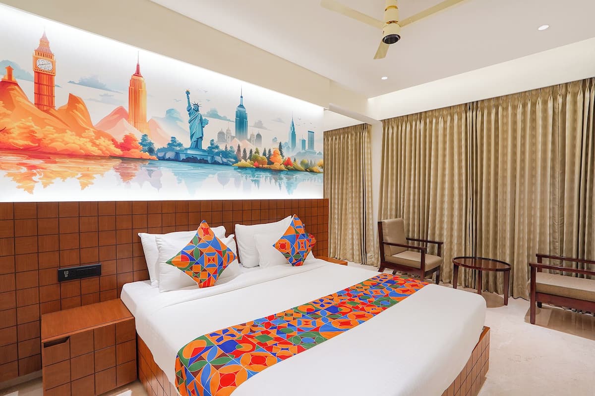 A hotel room with a large bed, a headboard with a cityscape mural, a desk, and a chair.