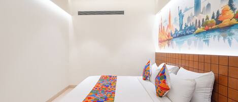 A hotel room with a large bed, white bedding, colorful pillows, a cityscape mural, and a modern ceiling design.
