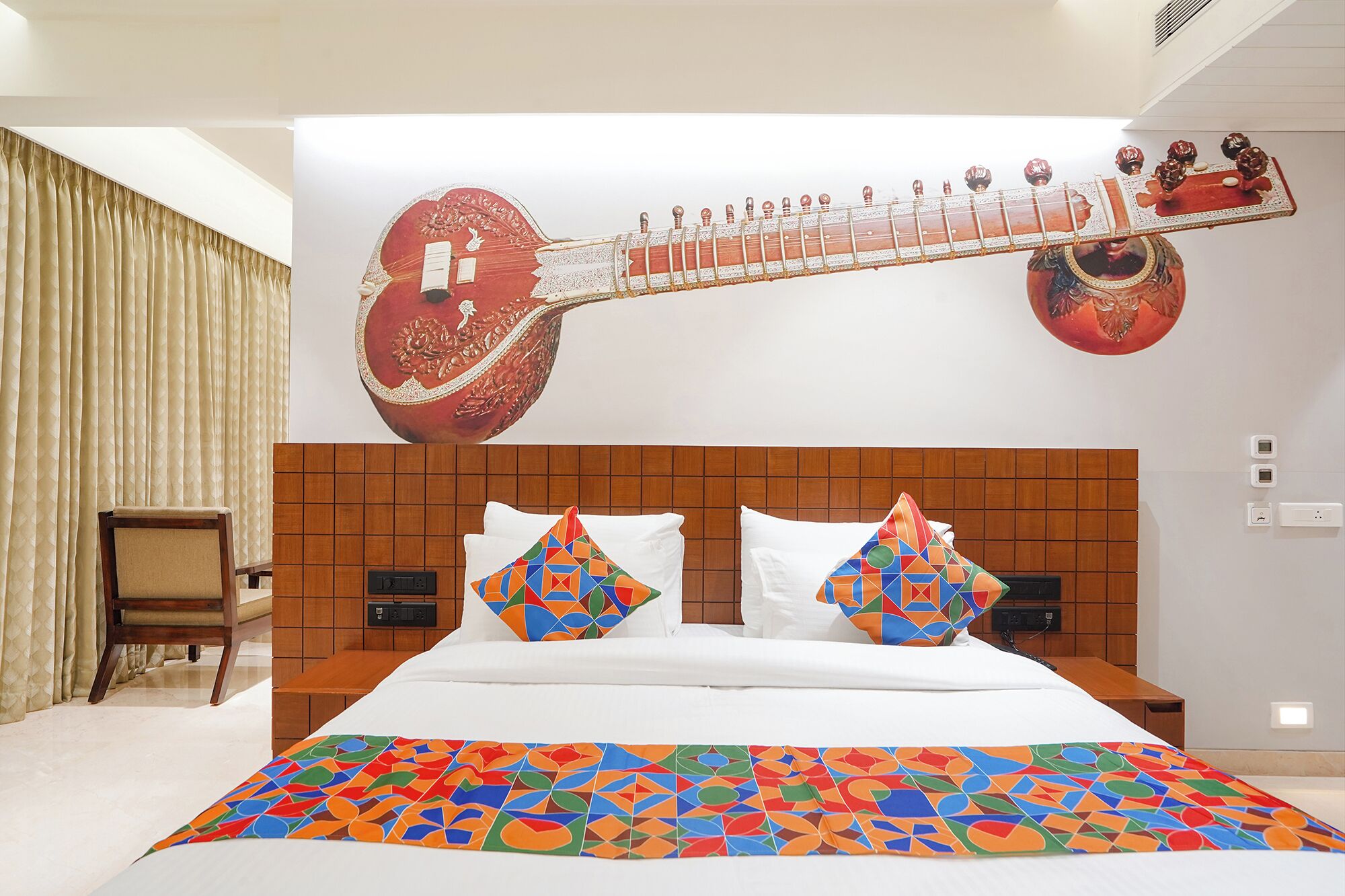 Une chambre d’hôtel avec un grand lit, deux tables de chevet, une tête de lit en bois et une fresque murale représentant un instrument à cordes.