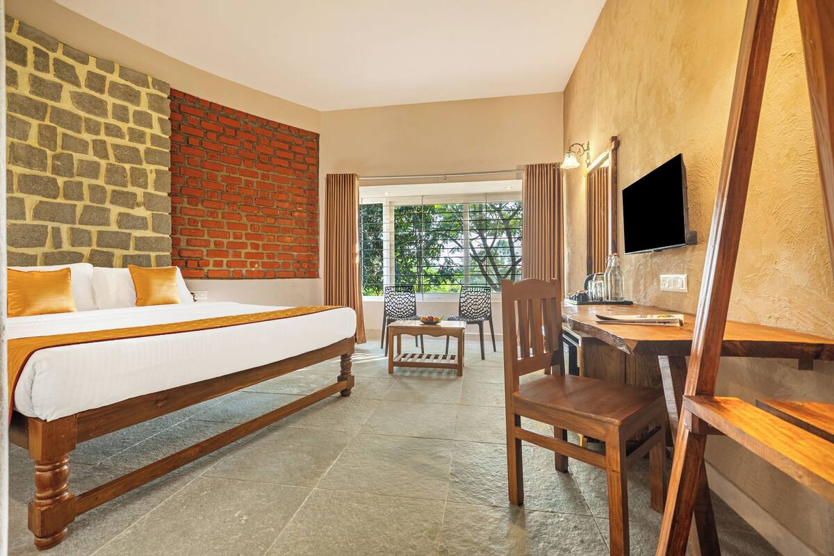 Habitación de hotel con cama, escritorio, silla, televisión y vistas a zonas verdes.