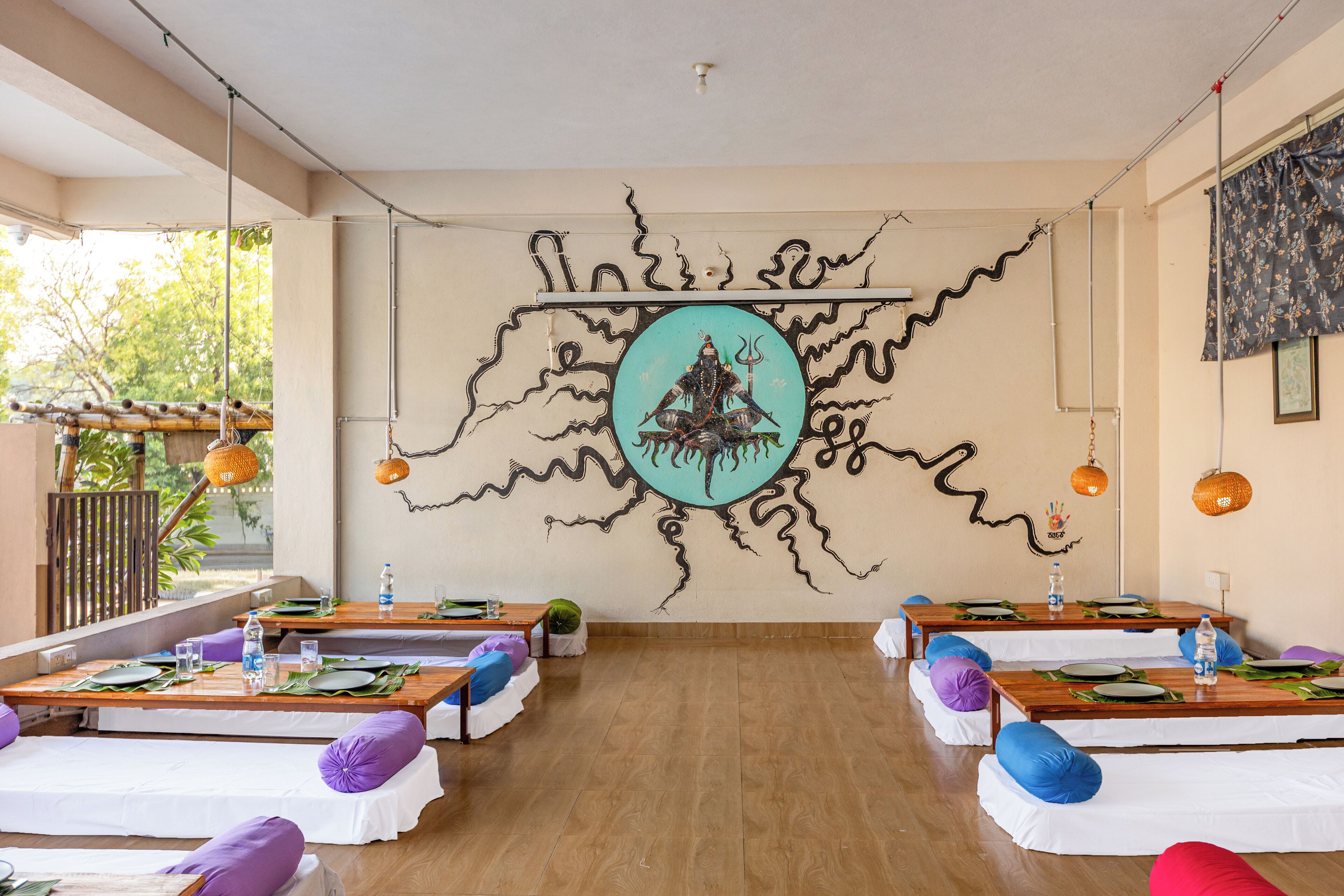 A dining area with tables set for two, each with white tablecloths, purple and blue cushions, and a central decorative piece.