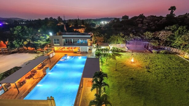 Ein Pool mit einer abgesenkten Liegefläche, umgeben von einer überdachten Sitzgruppe und einem Gebäude mit vielen Fenstern.